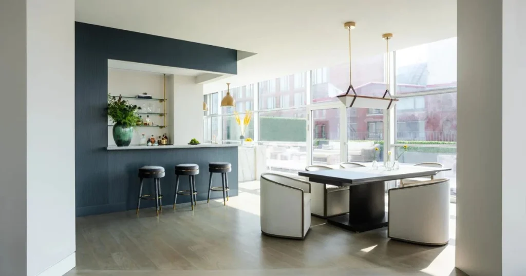 a sunlit, open-plan kitchen featuring a deep blue accent wall, floating shelves, a sleek island with geometric pendant lights, and contemporary bar stools