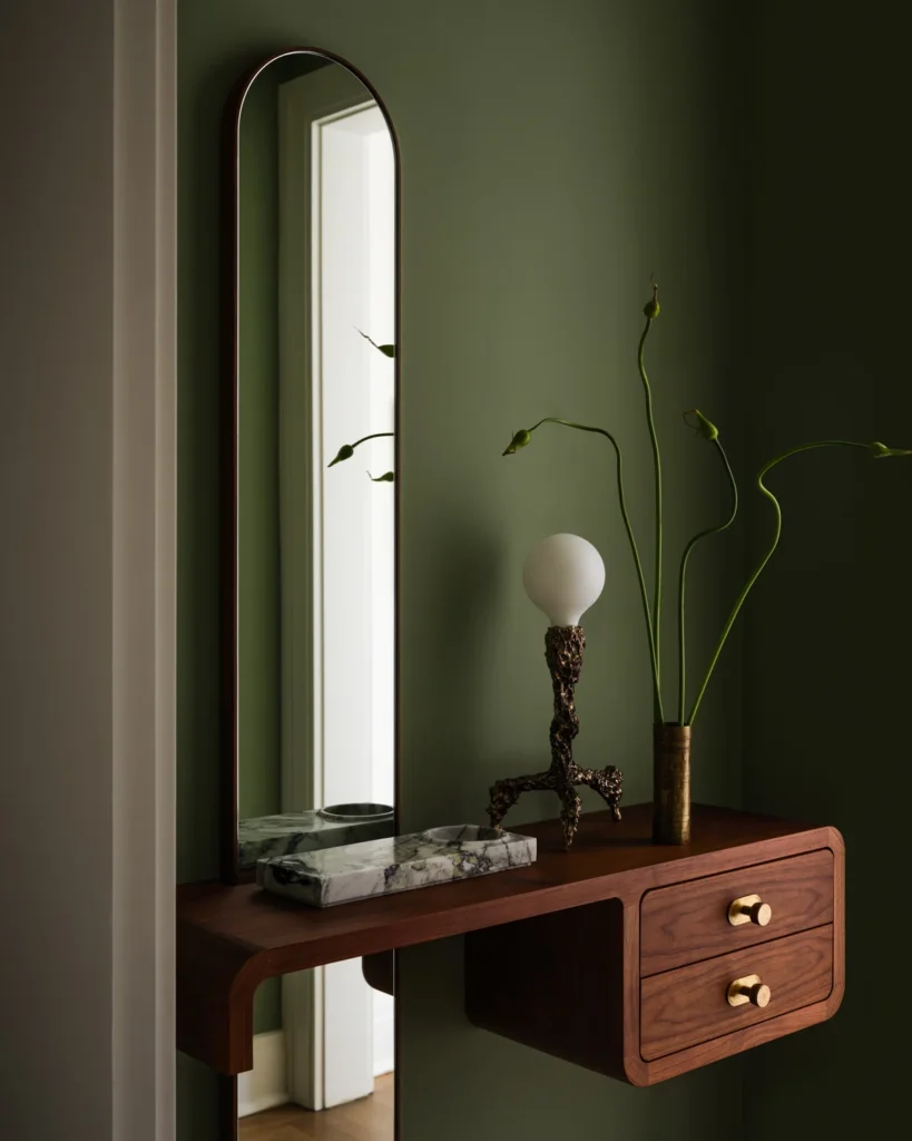 Home office with a wood desk, black metal shelving, sculptural wood lamp and green ombré curtains.
