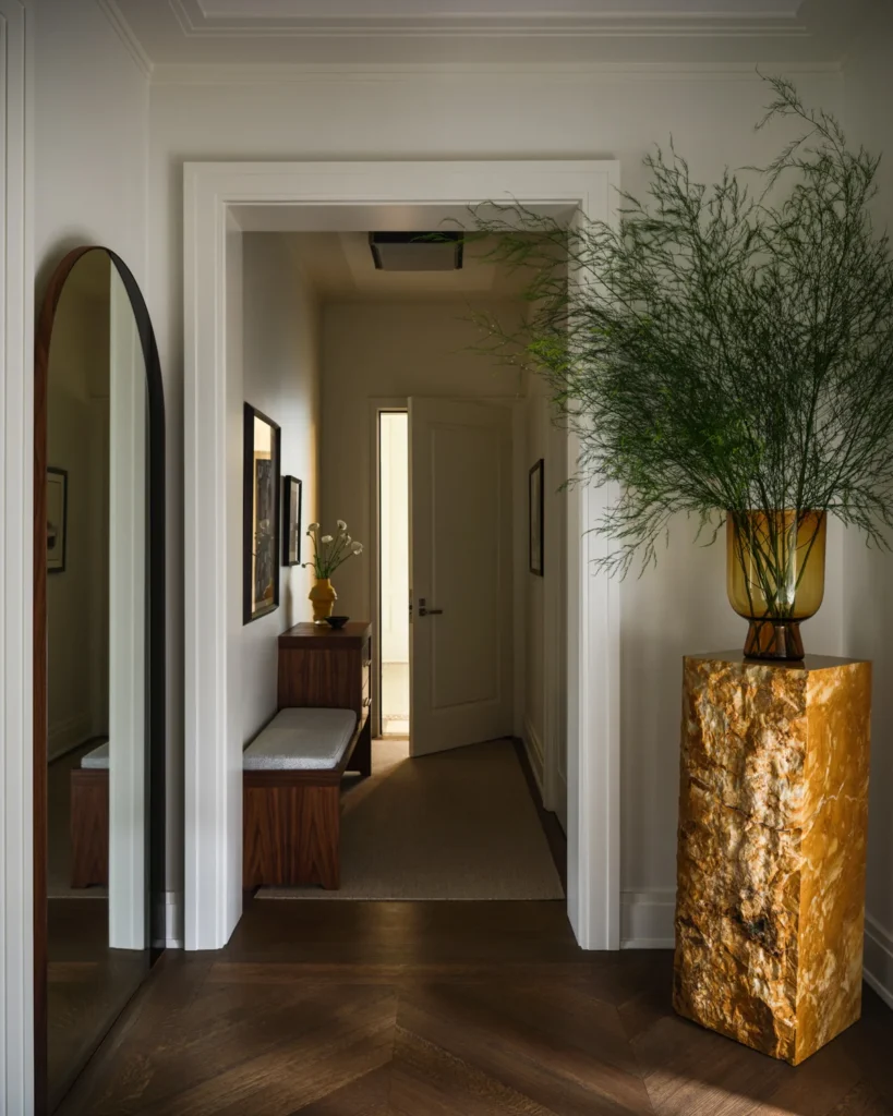 Custom walnut console with brass knobs, a tall mirror and sculptural lamp against an olive green wall.