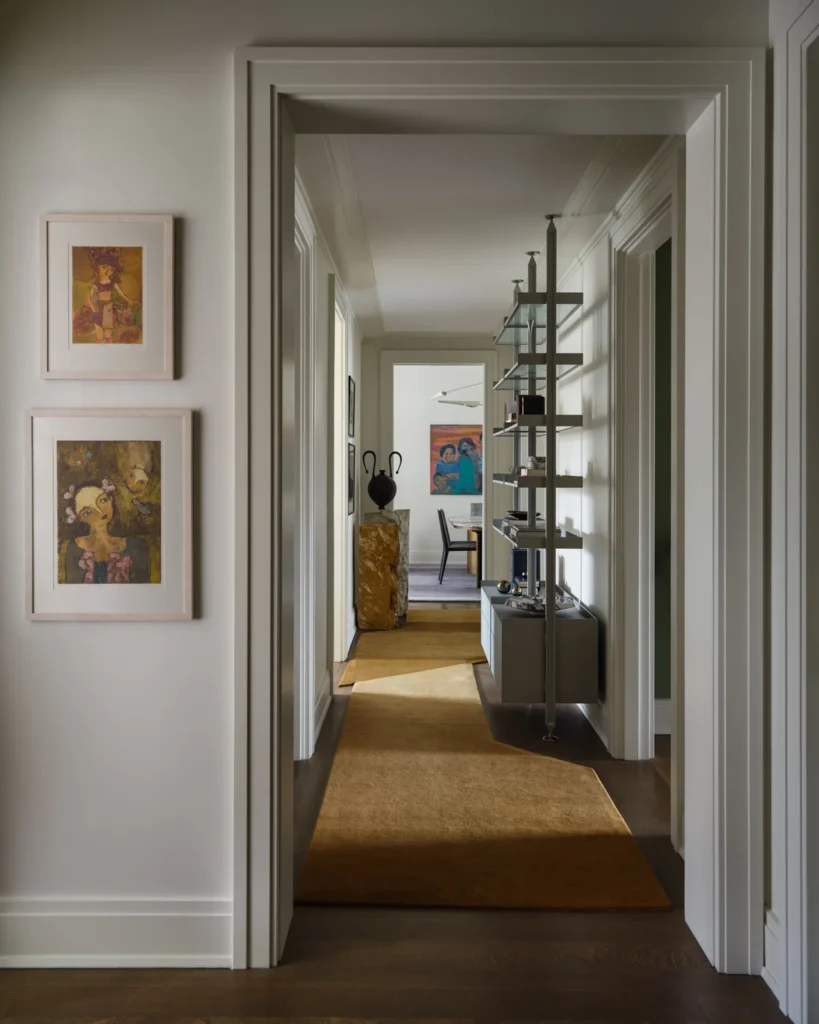 Belnord hallway with a custom ocher runner, floor-to-ceiling bookshelves and framed art leading toward the dining room.