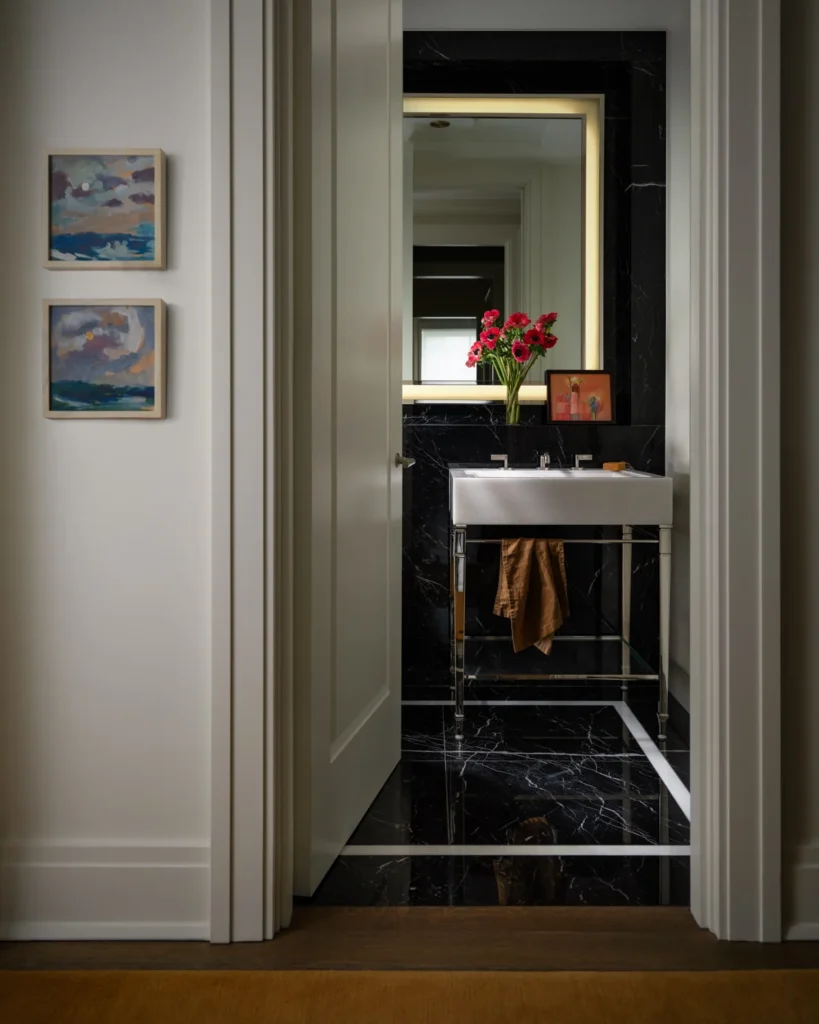 Black marble powder room styled with red flowers, a small framed painting and a warm brown hand towel.