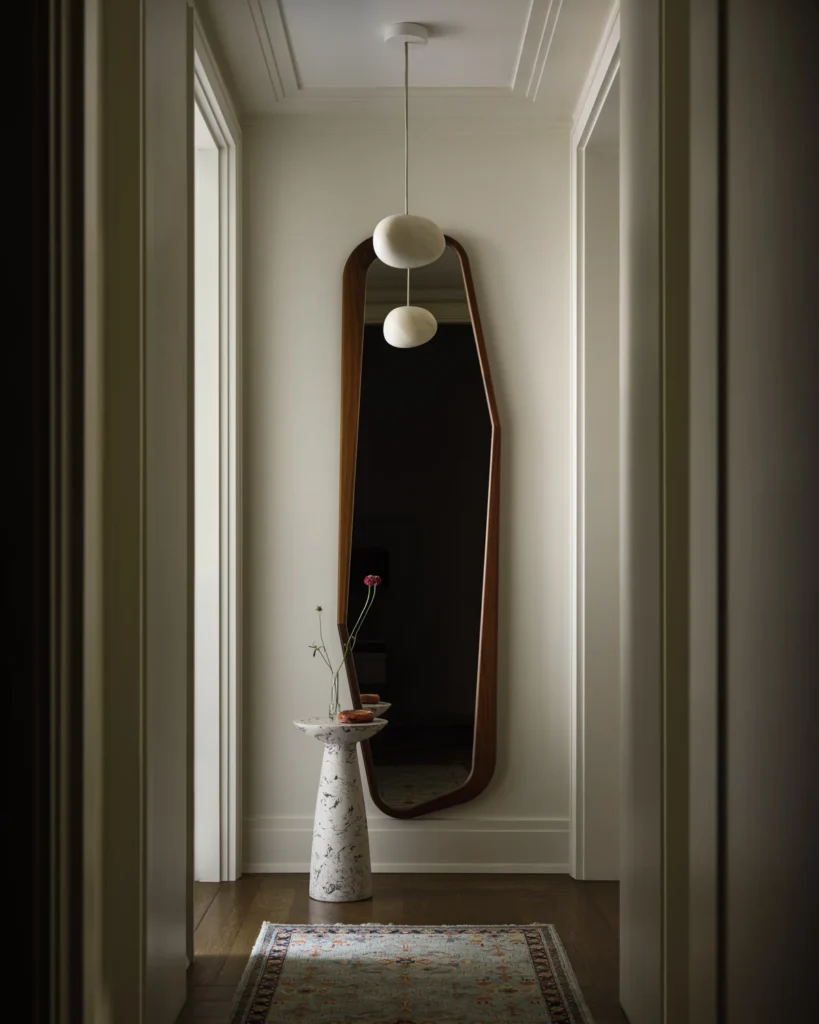 Hallway with an irregular wood-framed mirror, white stone pedestal table and patterned runner.
