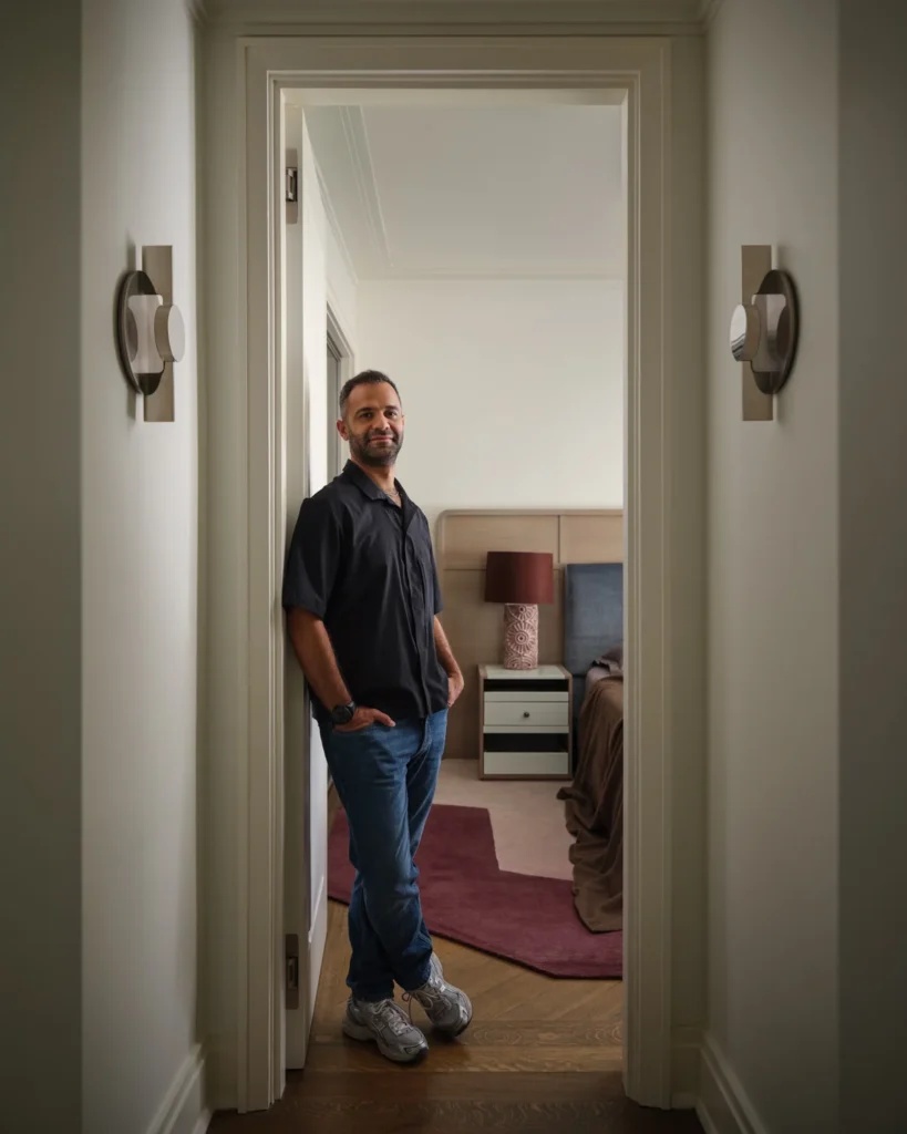 Ahmad standing in the Belnord bedroom doorway, with a custom walnut headboard and burgundy rug behind him.
