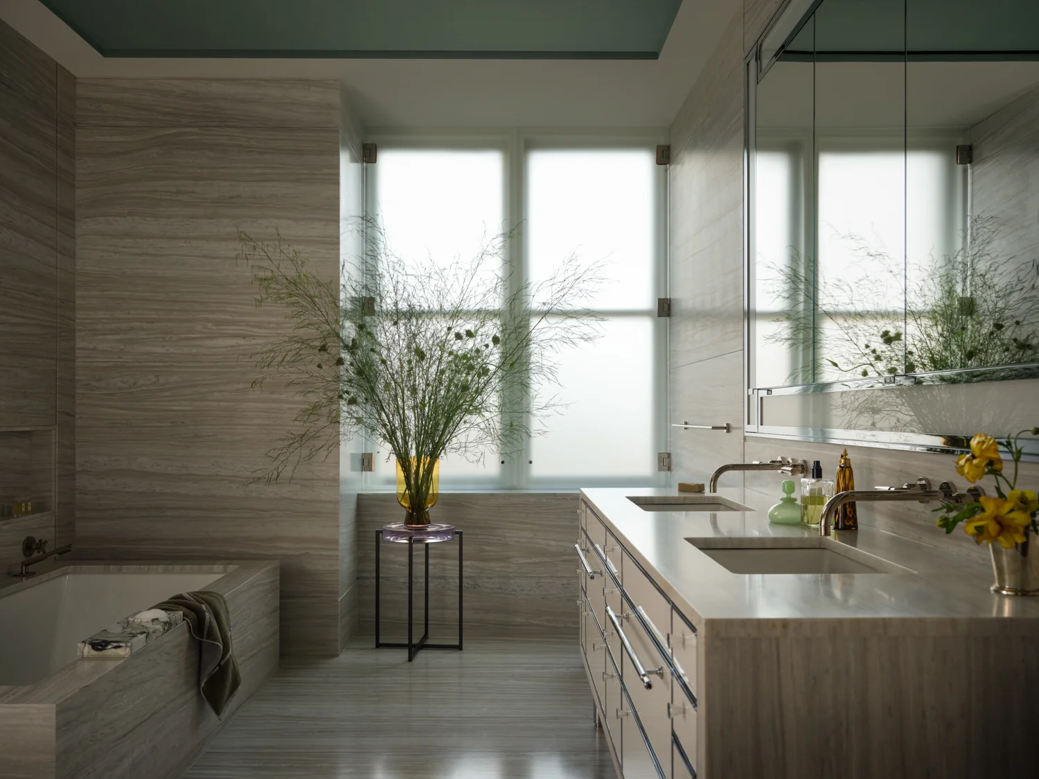 Bathroom styled with tall greenery in an amber vase, yellow flowers and colorful glass bottles.
